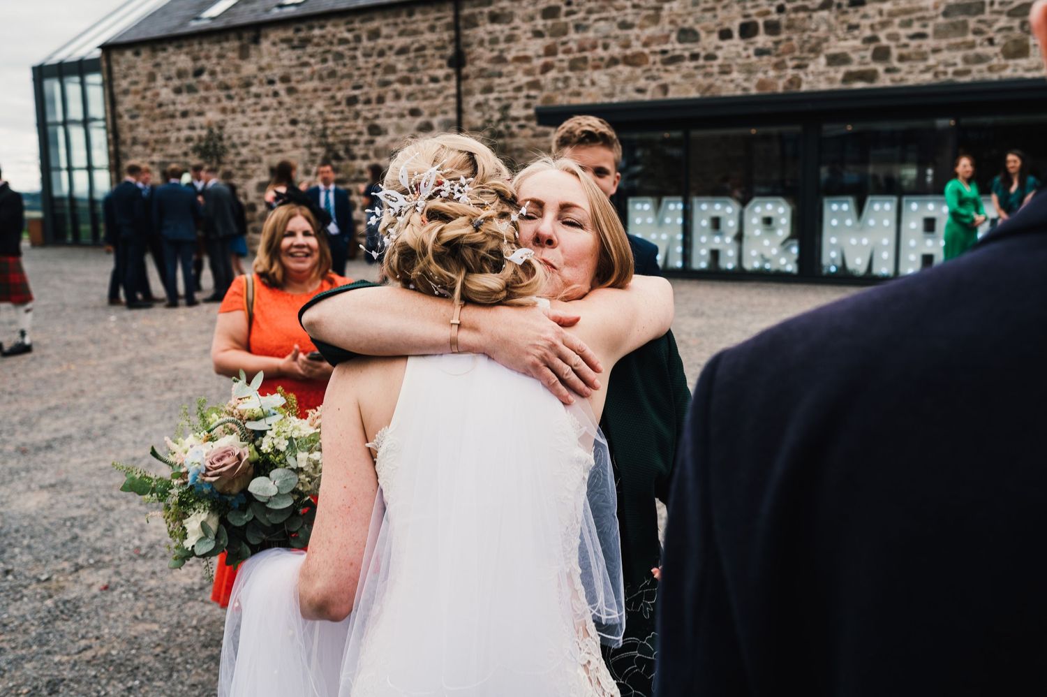 Emotional embrace shared during wedding reception near stone building with Mr & Mr sign.