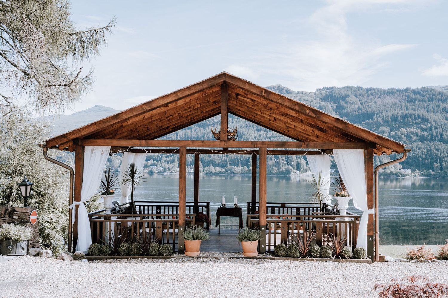 A wooden pavilion overlooking a serene mountain lake with snow-capped peaks in the background.