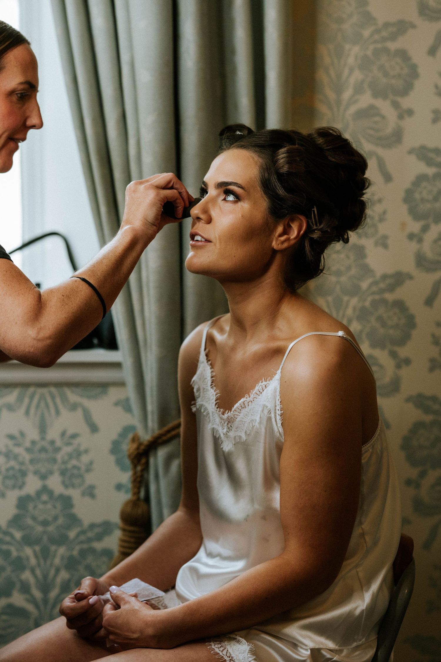 Bride getting ready in elegant room with damask wallpaper and curtains.