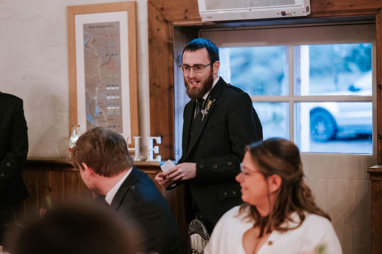 Wedding guests gathered at a reception venue with wood paneled walls and framed photos.