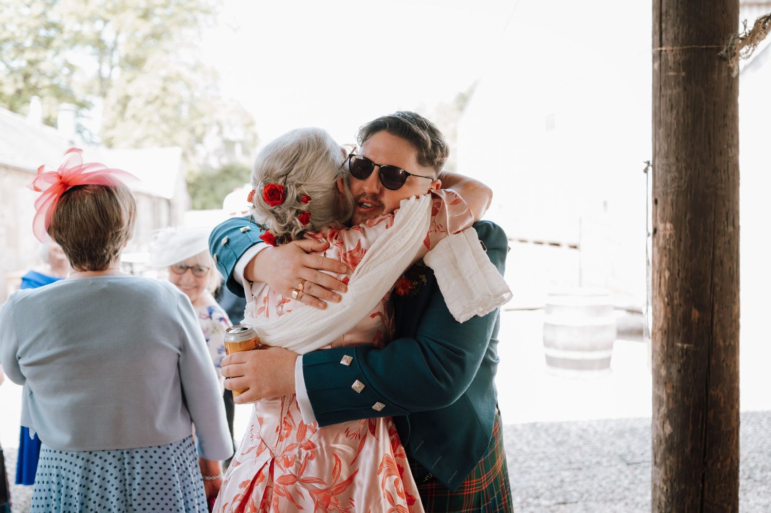 Wedding guests embrace at outdoor celebration with traditional Scottish attire.