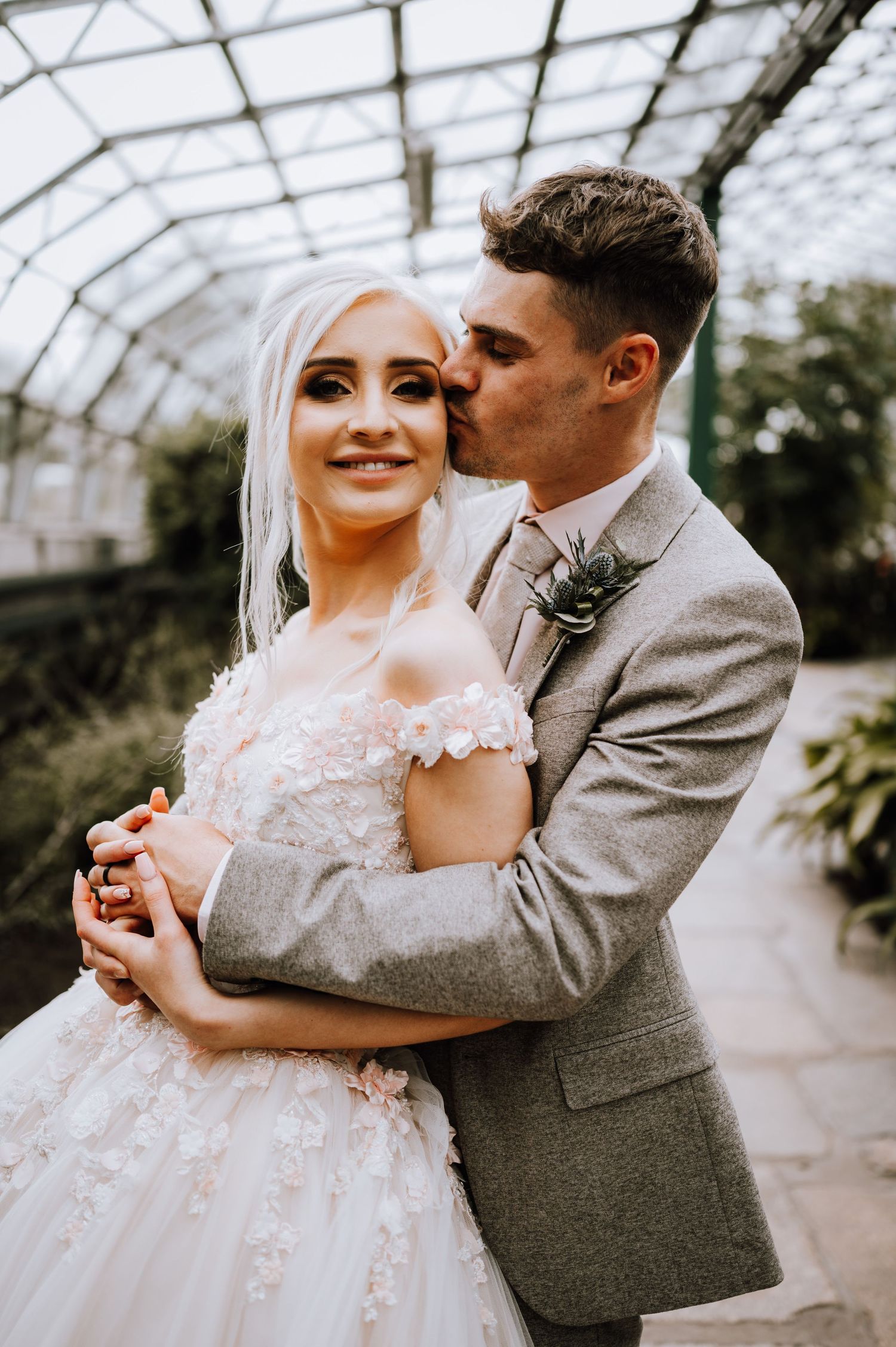 An intimate wedding moment captured in a greenhouse with dreamy natural light filtering through.
