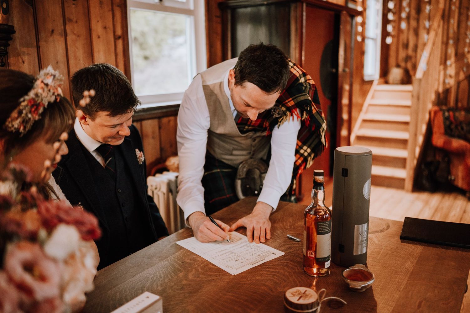 Wedding party gathered around wooden table for document signing with wine glasses and candles.