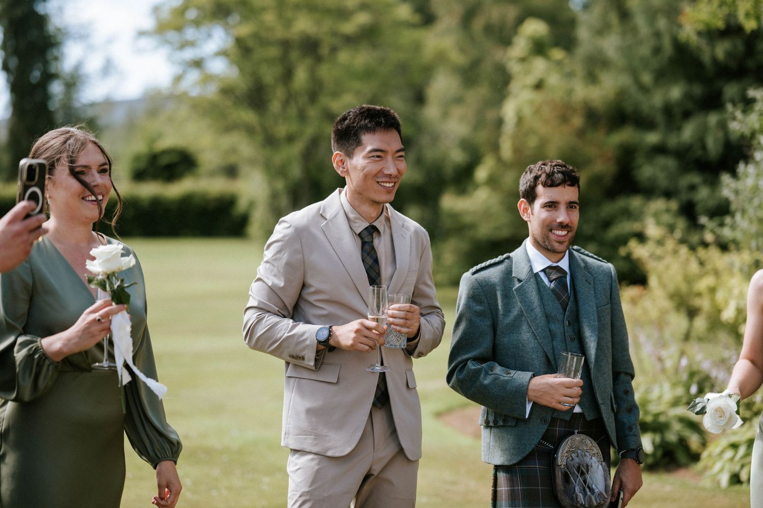 Wedding guests mingling and enjoying drinks on a sunny lawn during an outdoor reception.