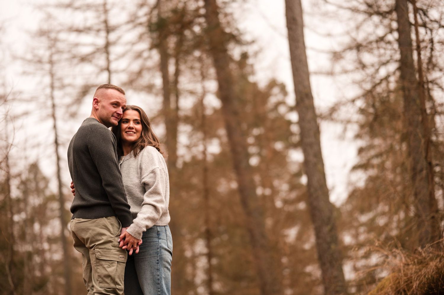 Engagement photography session Aberdeen. A couple embraces in a sepia-toned forest setting.