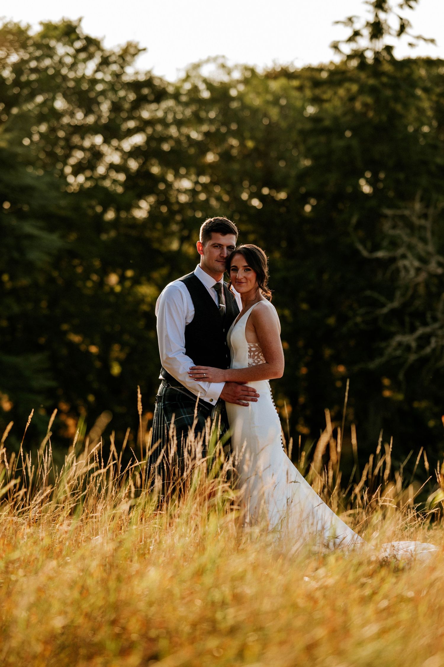 Aberdeen Wedding Photography. Newlyweds embrace in golden field during sunset photo session.
