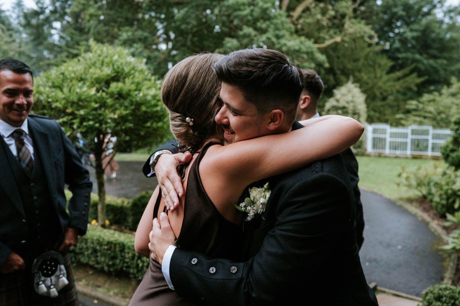 Wedding guests embracing outdoors on a lush green garden path.