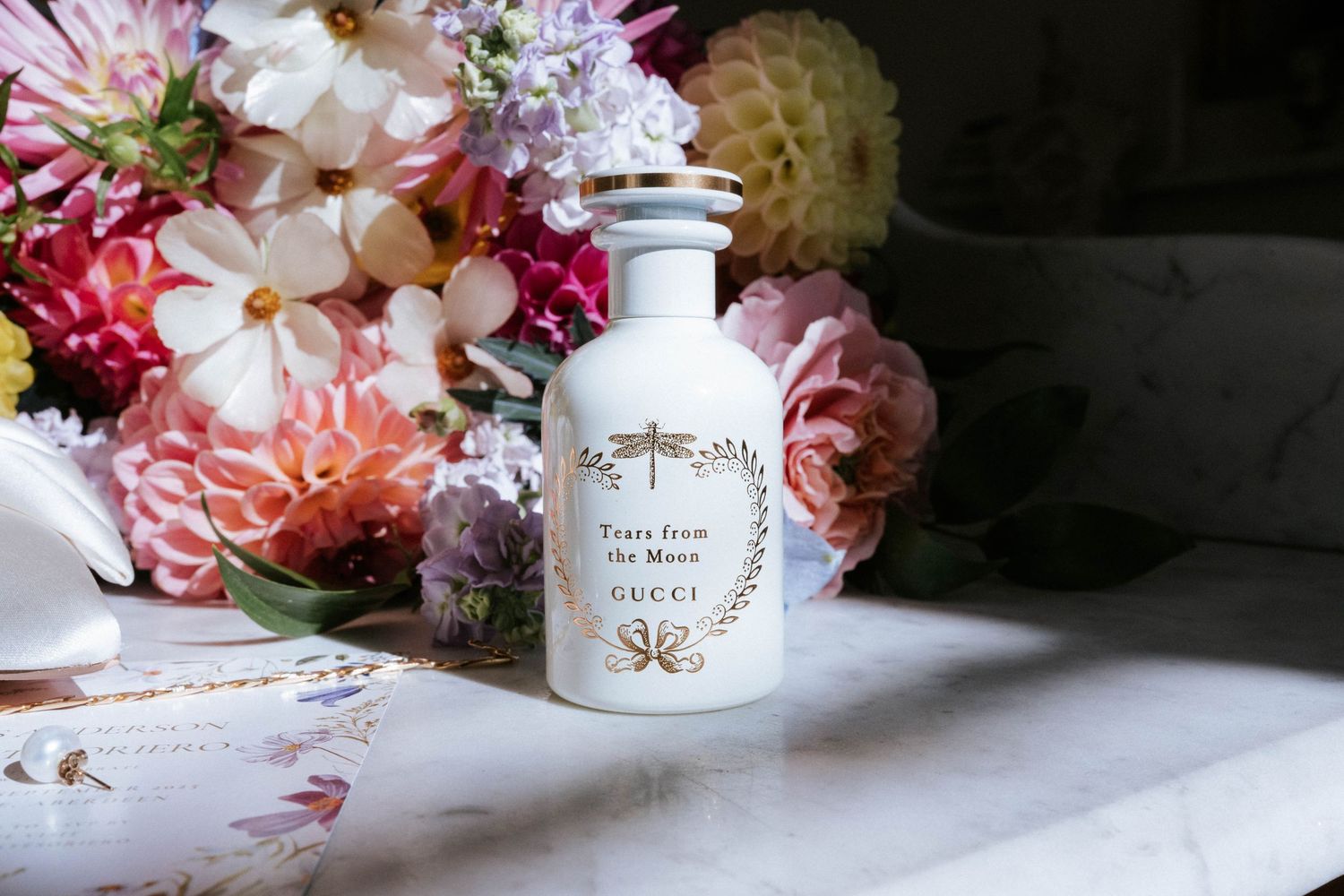 Elegant pink and white flowers arranged next to perfume bottles and beauty products on a light surface.