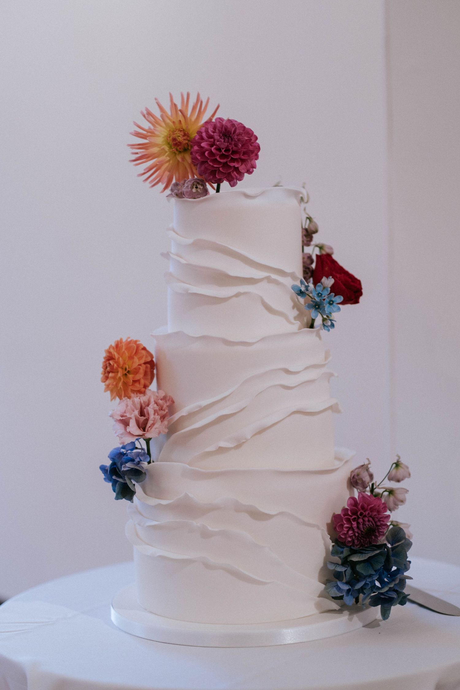 White textured wedding cake decorated with colorful fresh flowers in orange, blue and pink.