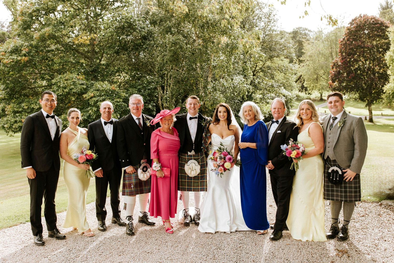 Extended wedding party in mix of formal wear and traditional Scottish dress posed in garden setting.