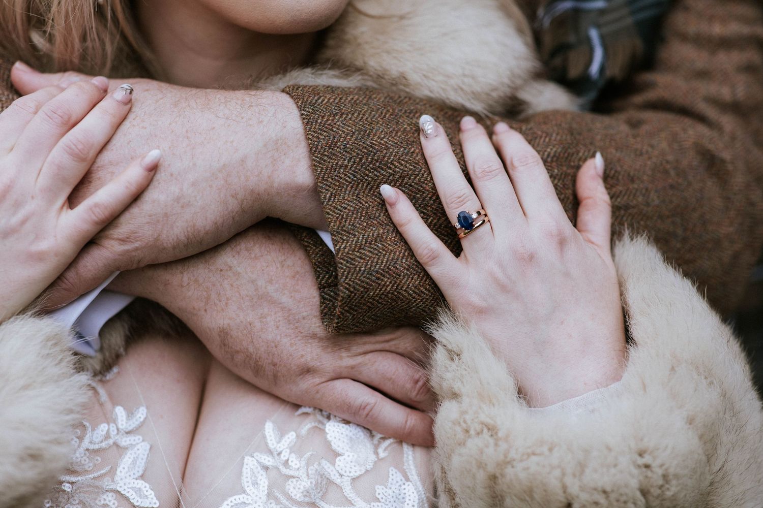 Close-up of hands wearing wedding rings against textured fabric and lace.