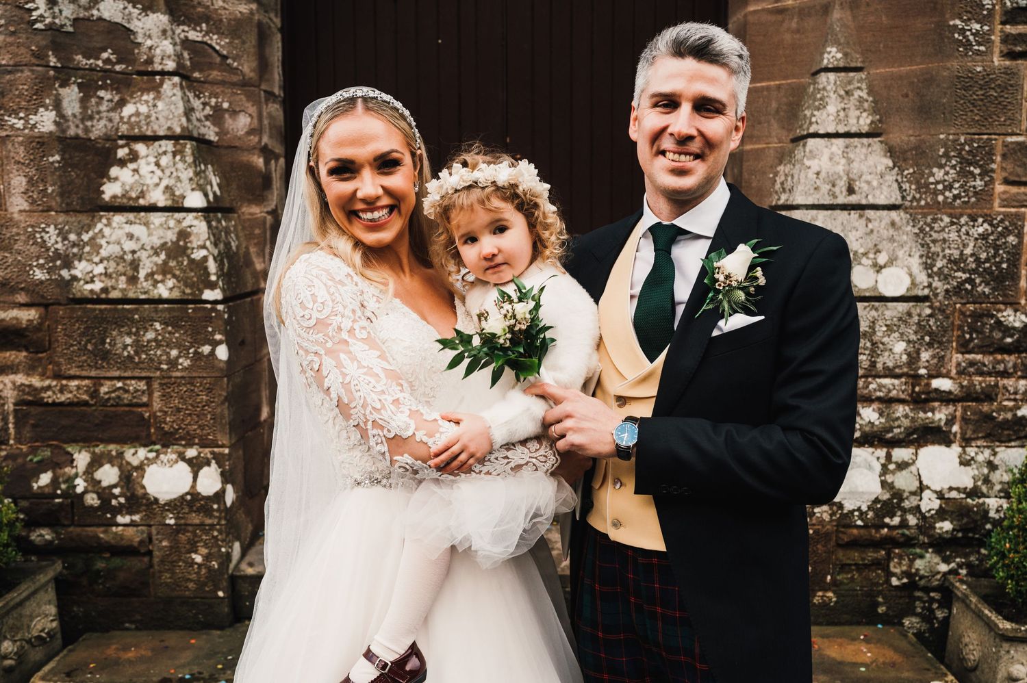 Wedding portrait at stone church entrance with bride in lace dress.