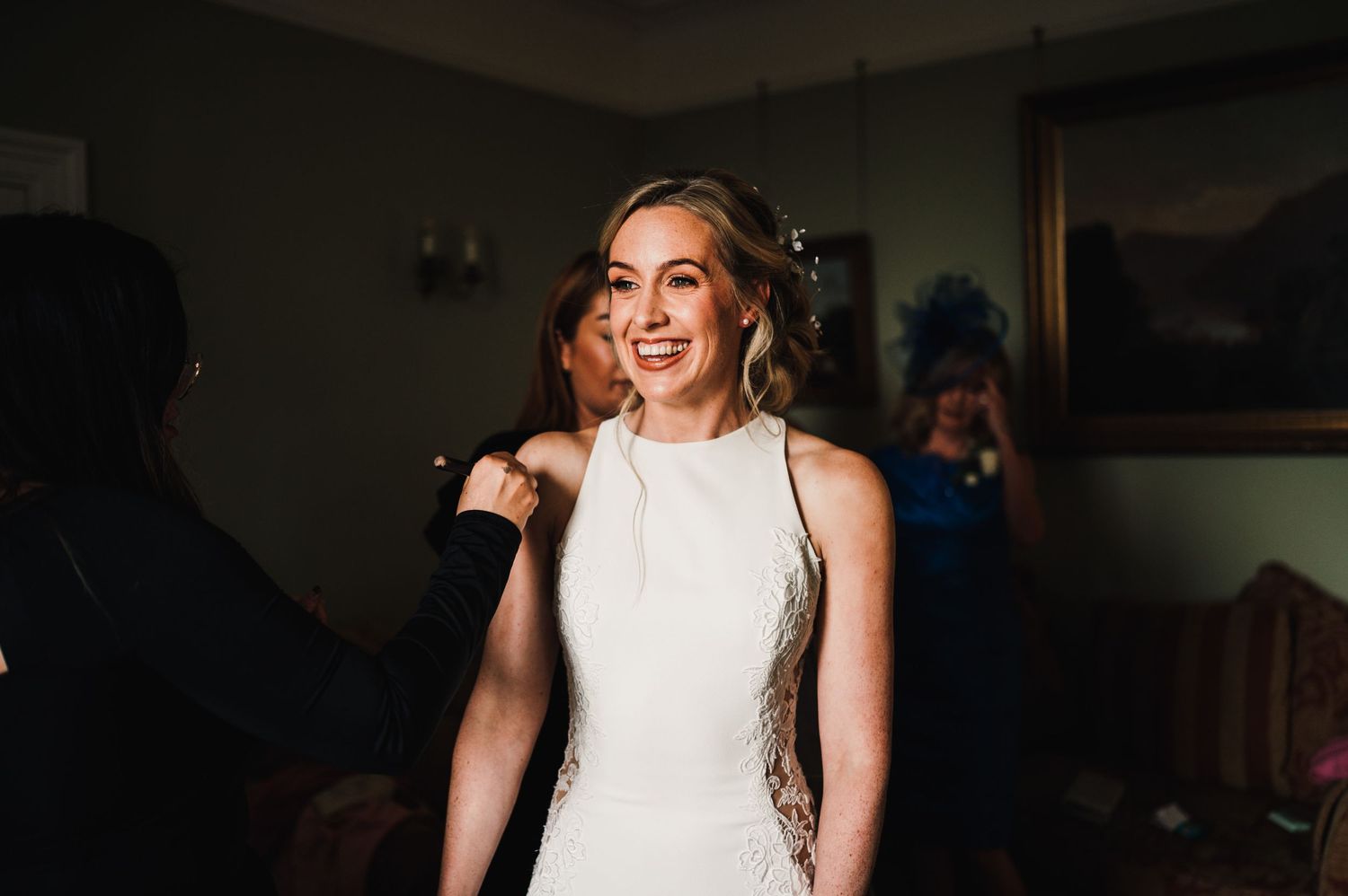 Someone wearing an elegant white wedding dress smiling during preparation.