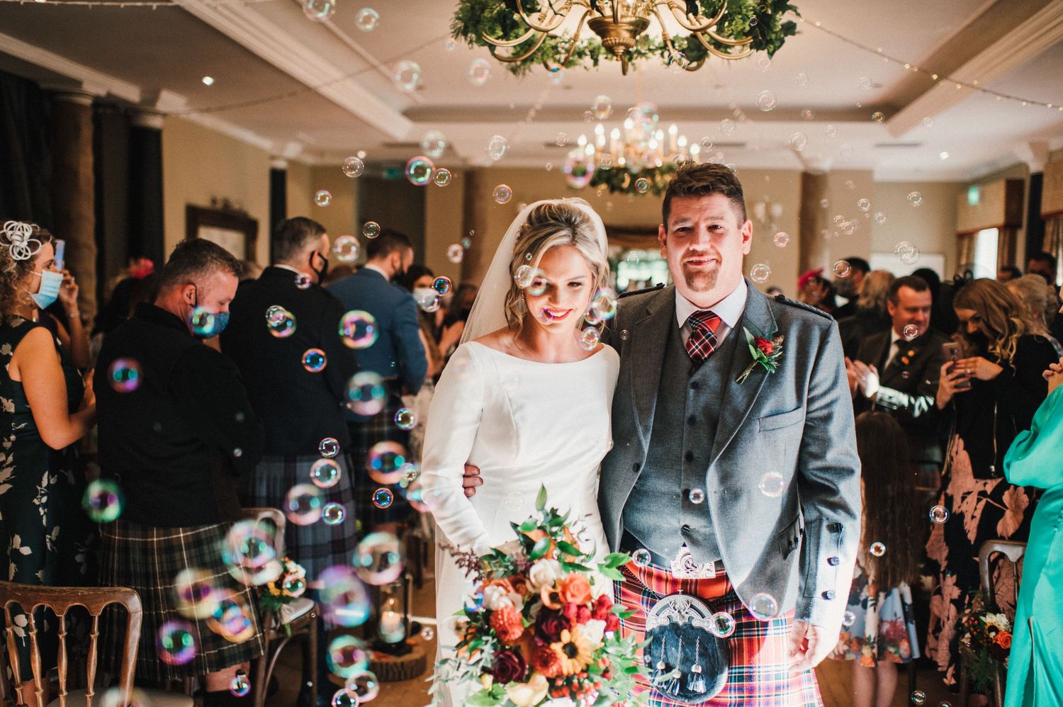 Joyful wedding couple surrounded by bubbles during their indoor celebration.