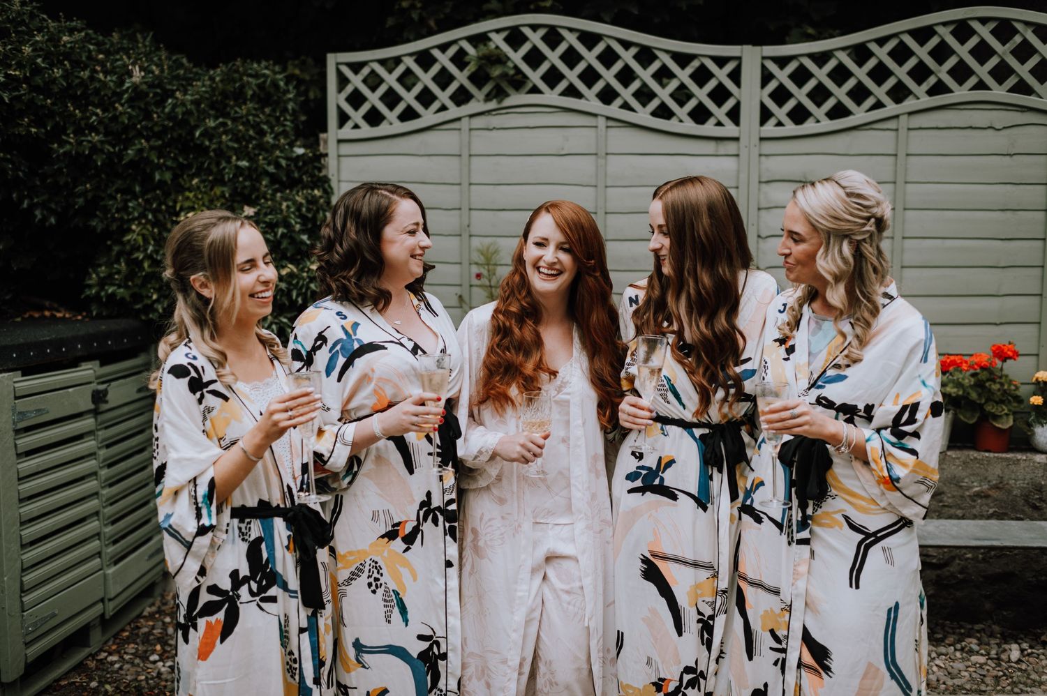 Wedding party in matching floral robes posing together in a garden setting.