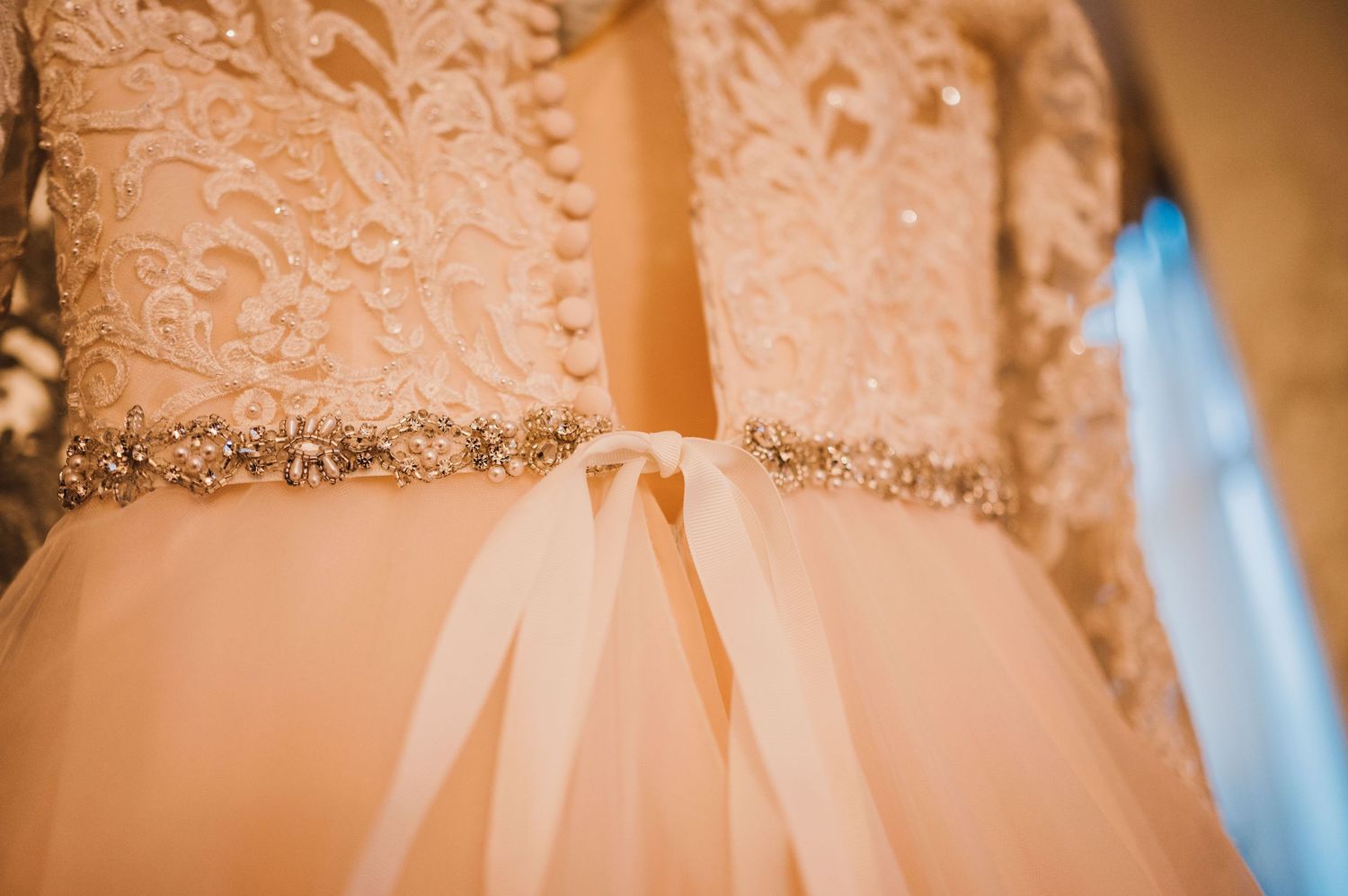 Close-up detail of a blush wedding dress with delicate beading and satin ribbon around the waist.