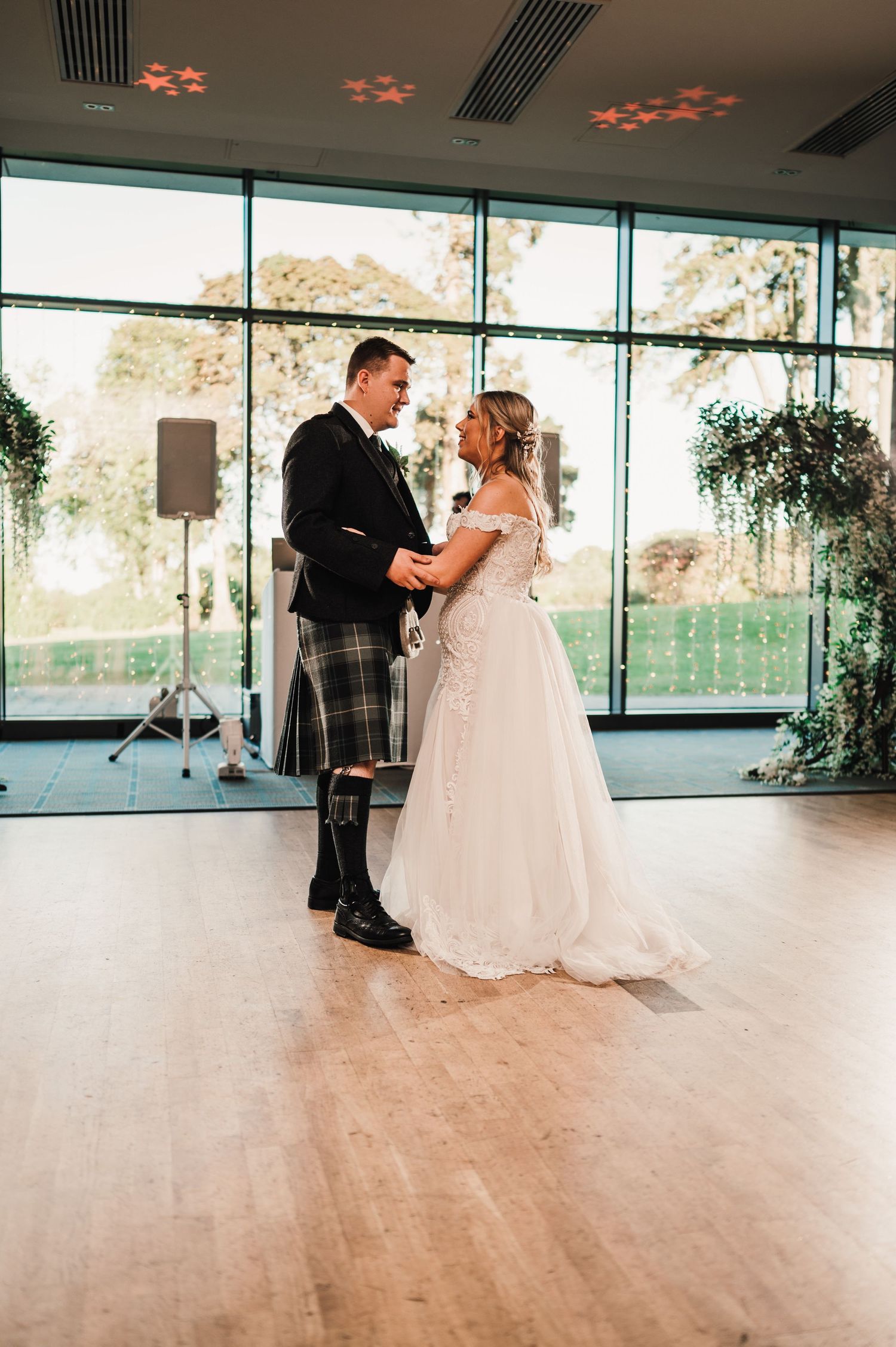 Couple sharing their first dance in a modern venue with Scottish wedding attire and floral decorations.