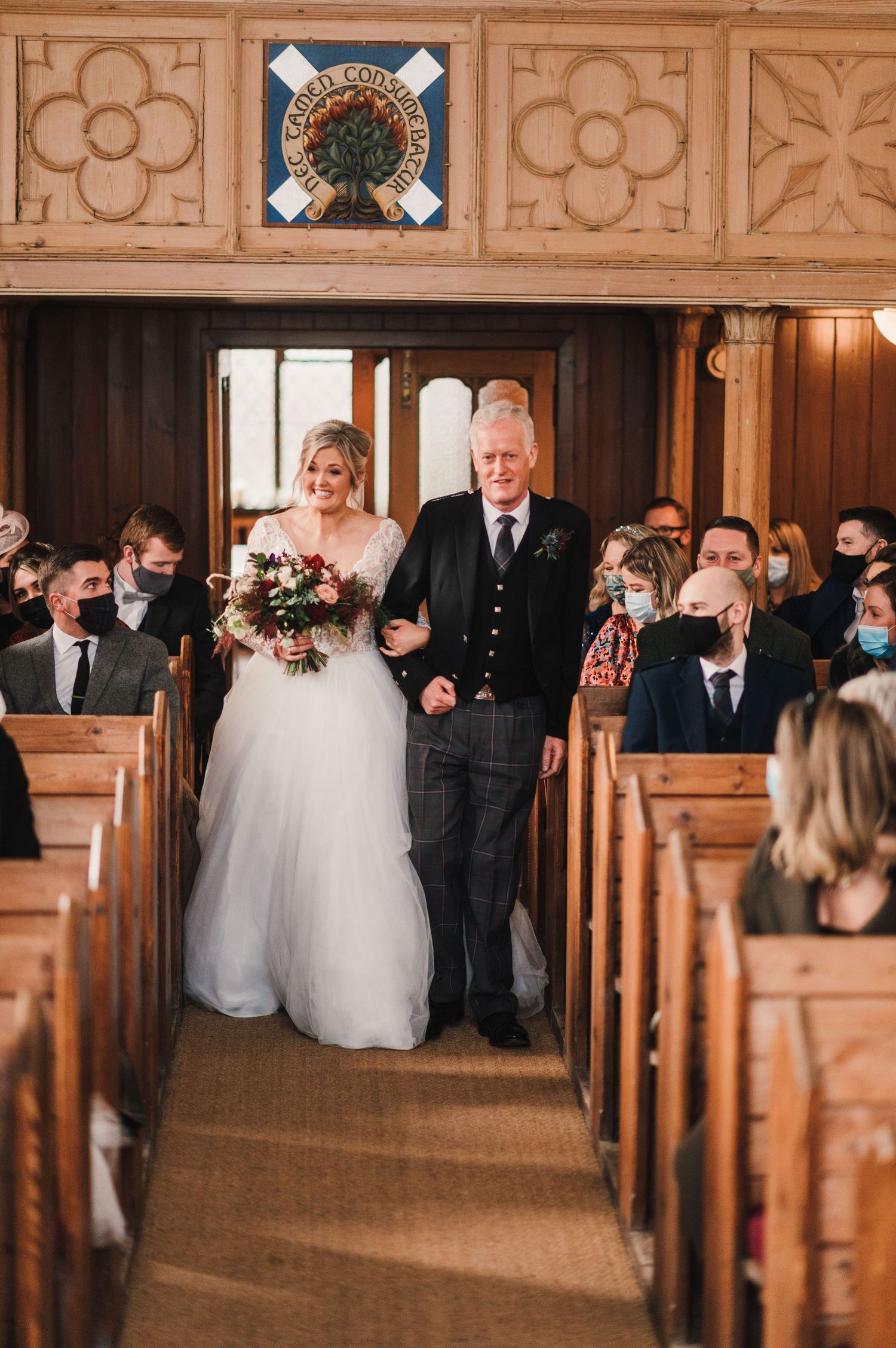 A procession down a church aisle with ornate wooden details and ceiling decorations.