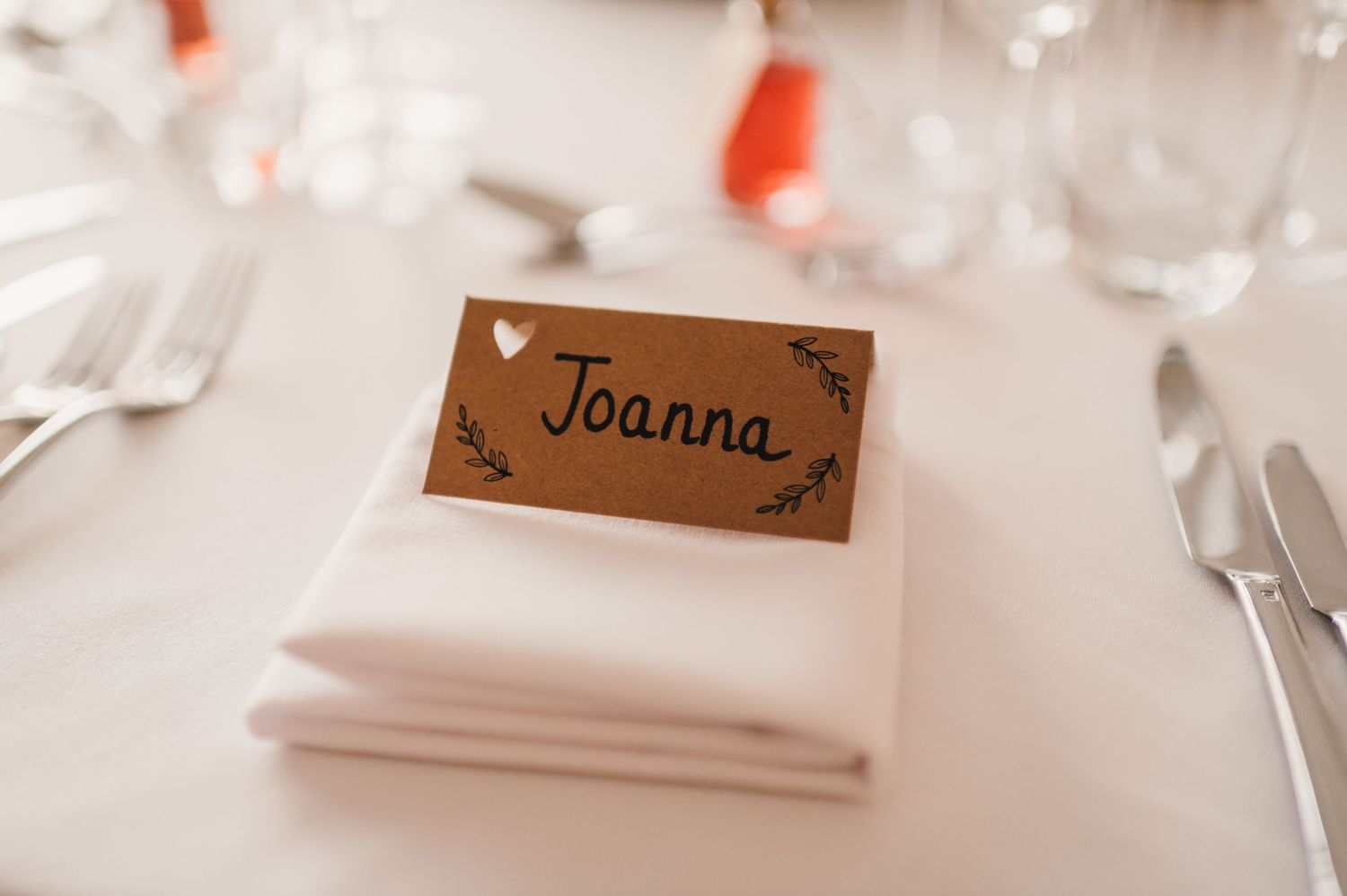 A wedding place card reading Joanna sits atop a white napkin at an elegant table setting.