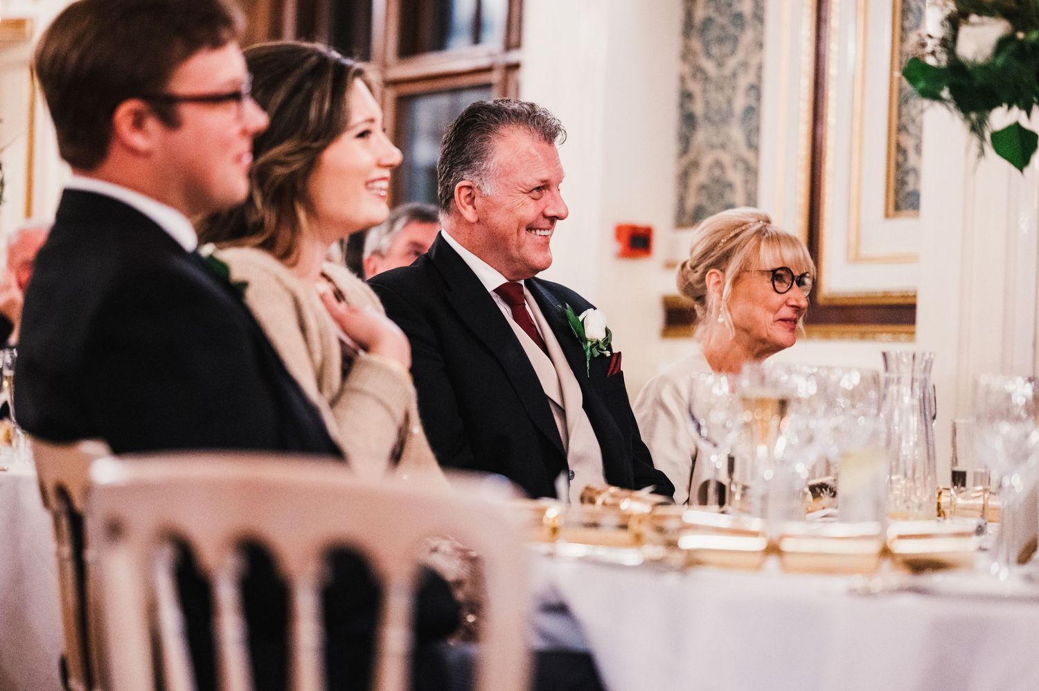 Wedding guests enjoying dinner conversation at an elegantly set reception table with wine glasses and decor.