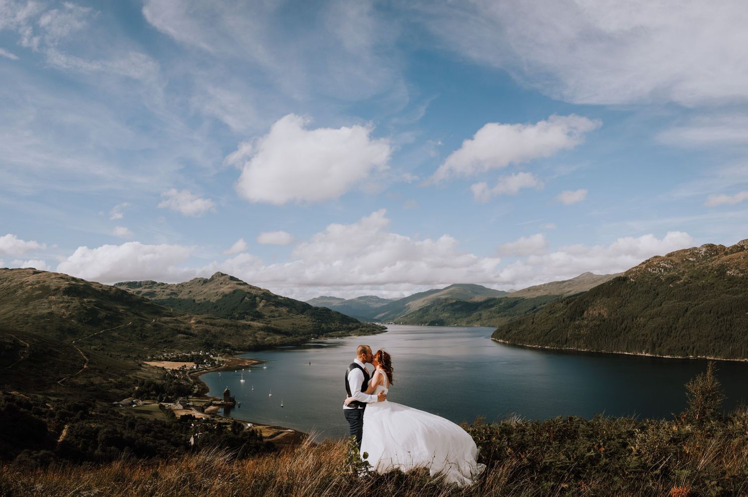 A dramatic wedding photo overlooking a Scottish loch with mountains in the distance.
