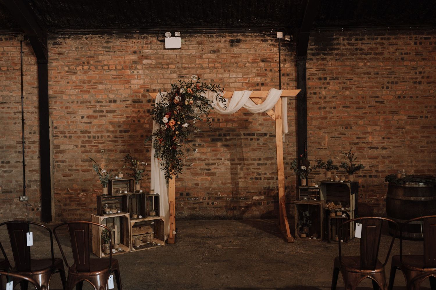 Wooden arch decorated with floral arrangements against exposed brick wall in industrial wedding venue.
