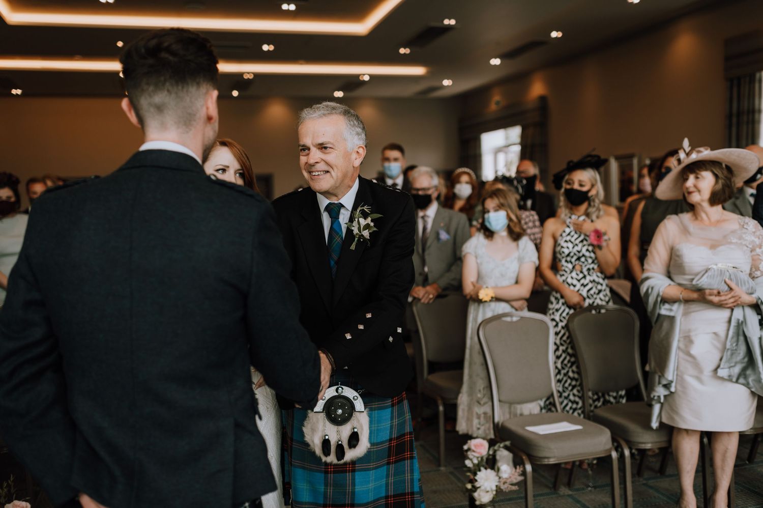 Scottish wedding ceremony with attendees in traditional kilts and formal attire.