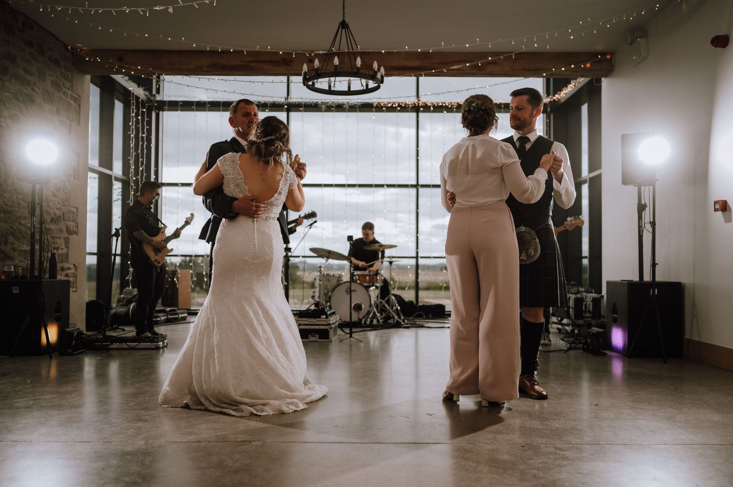 Wedding reception with dancing couples and live band in a modern venue with panoramic windows.
