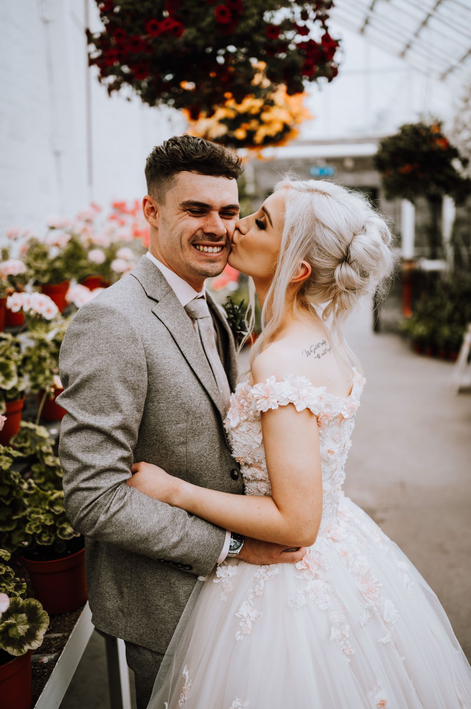 Joyful wedding portrait in a greenhouse with red flowers and natural lighting.