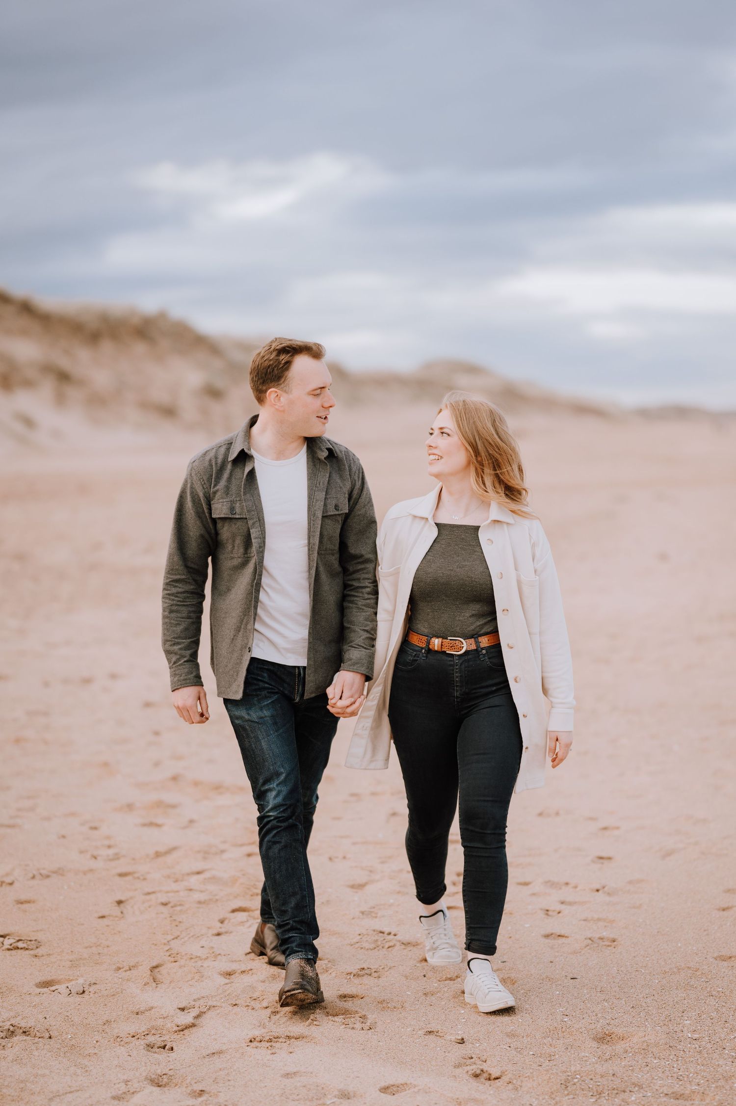 A silhouetted couple stands atop sandy dunes against dramatic cloudy skies.