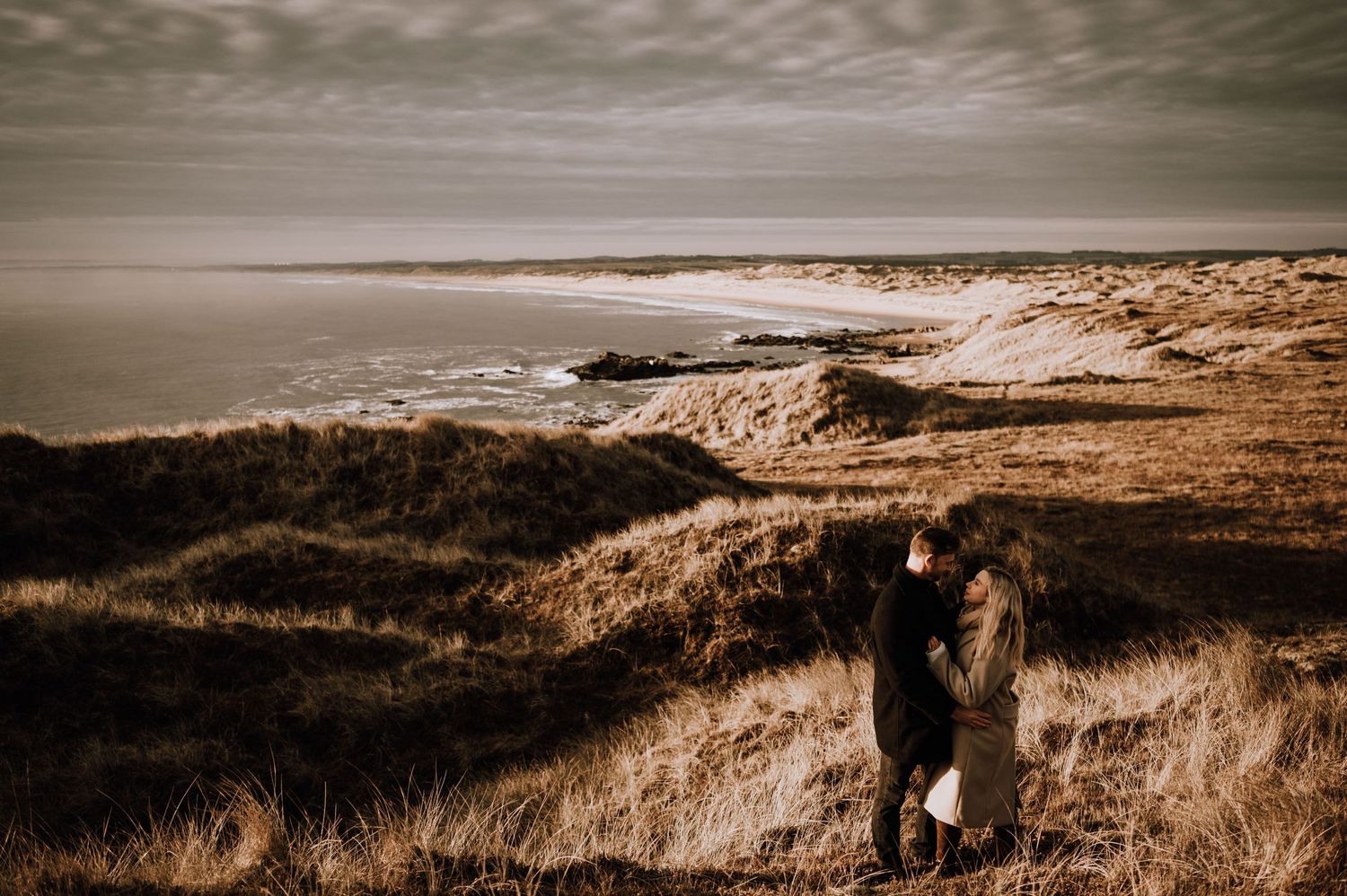 A romantic silhouette against a dramatic coastal landscape with rolling hills and ocean views.