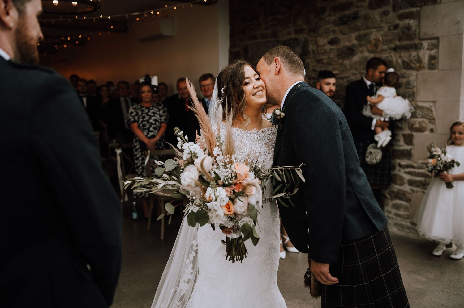Romantic moment during wedding ceremony in rustic venue with stone walls and ambient lighting.