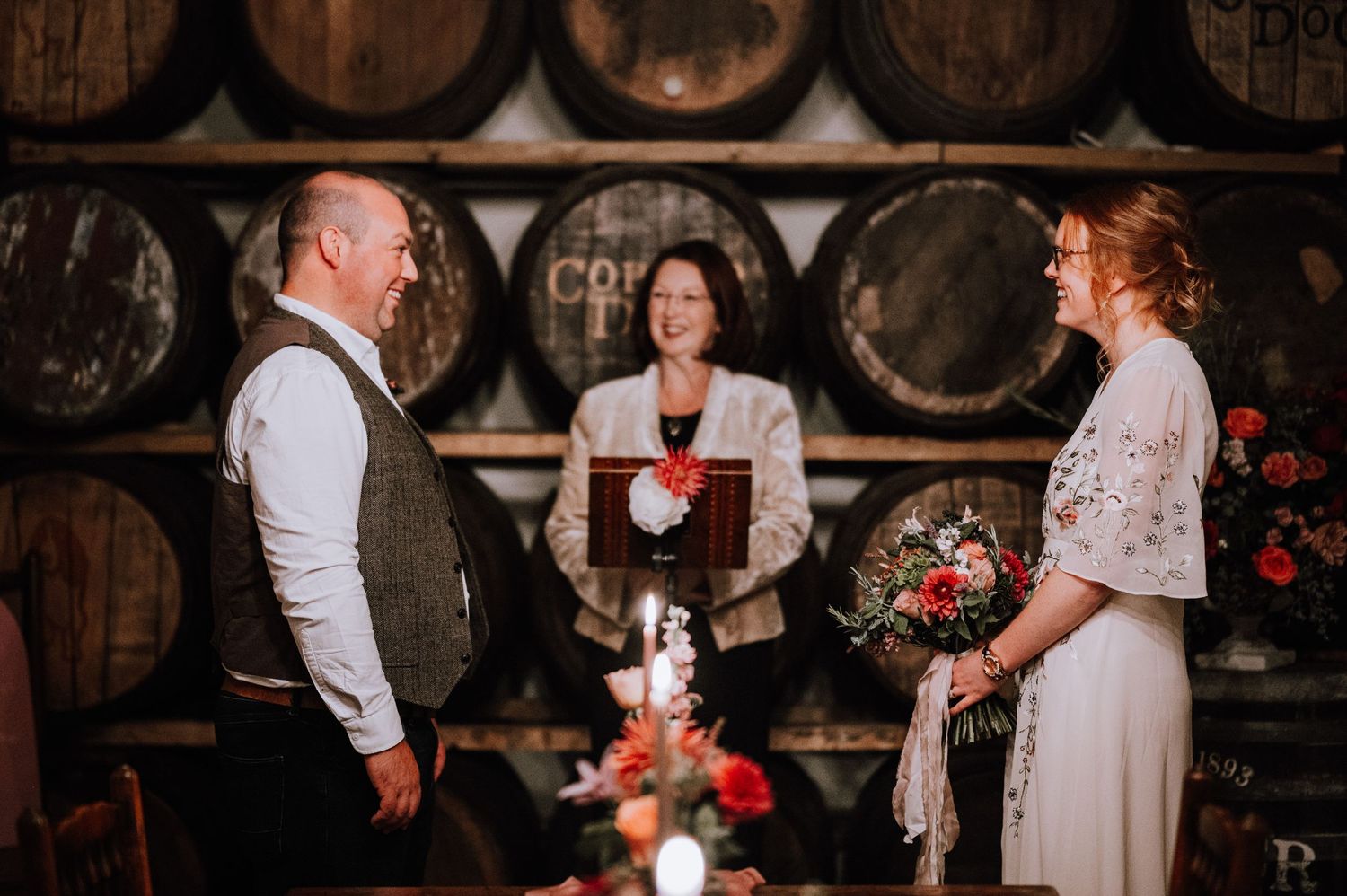 Intimate wedding ceremony taking place in front of stacked wine barrels with candlelight.