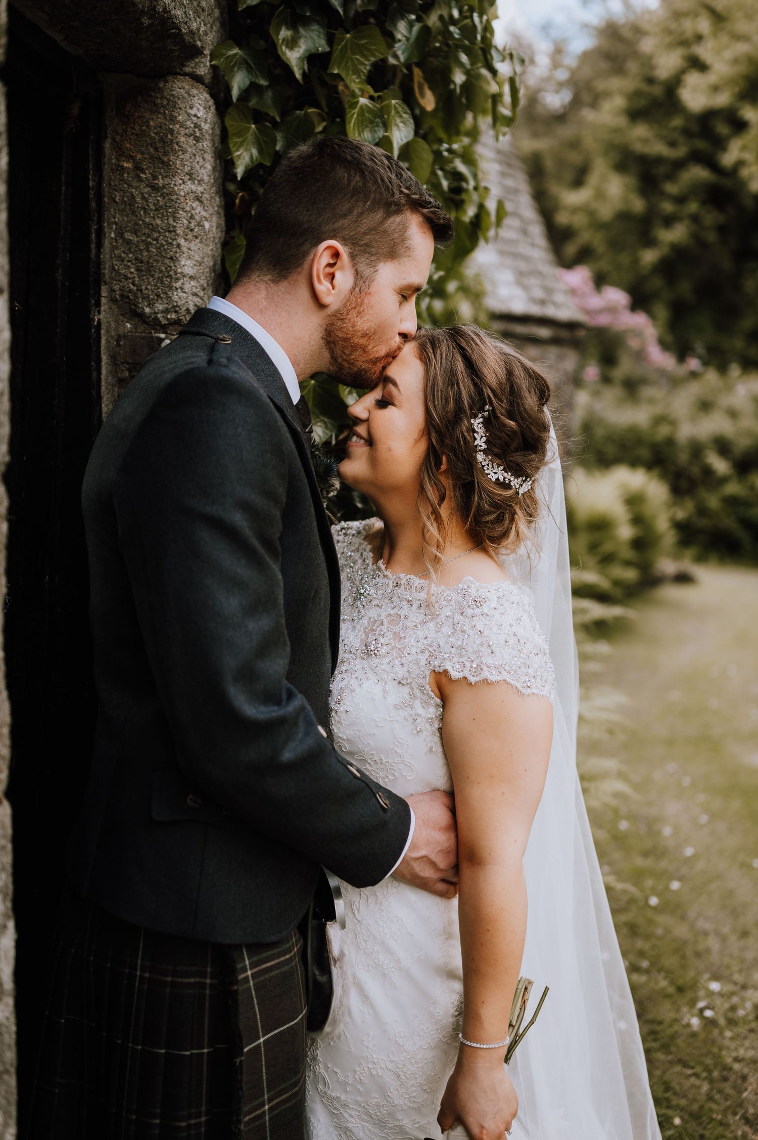 Intimate wedding portrait against a stone wall with ivy showing Scottish and traditional bridal styling.