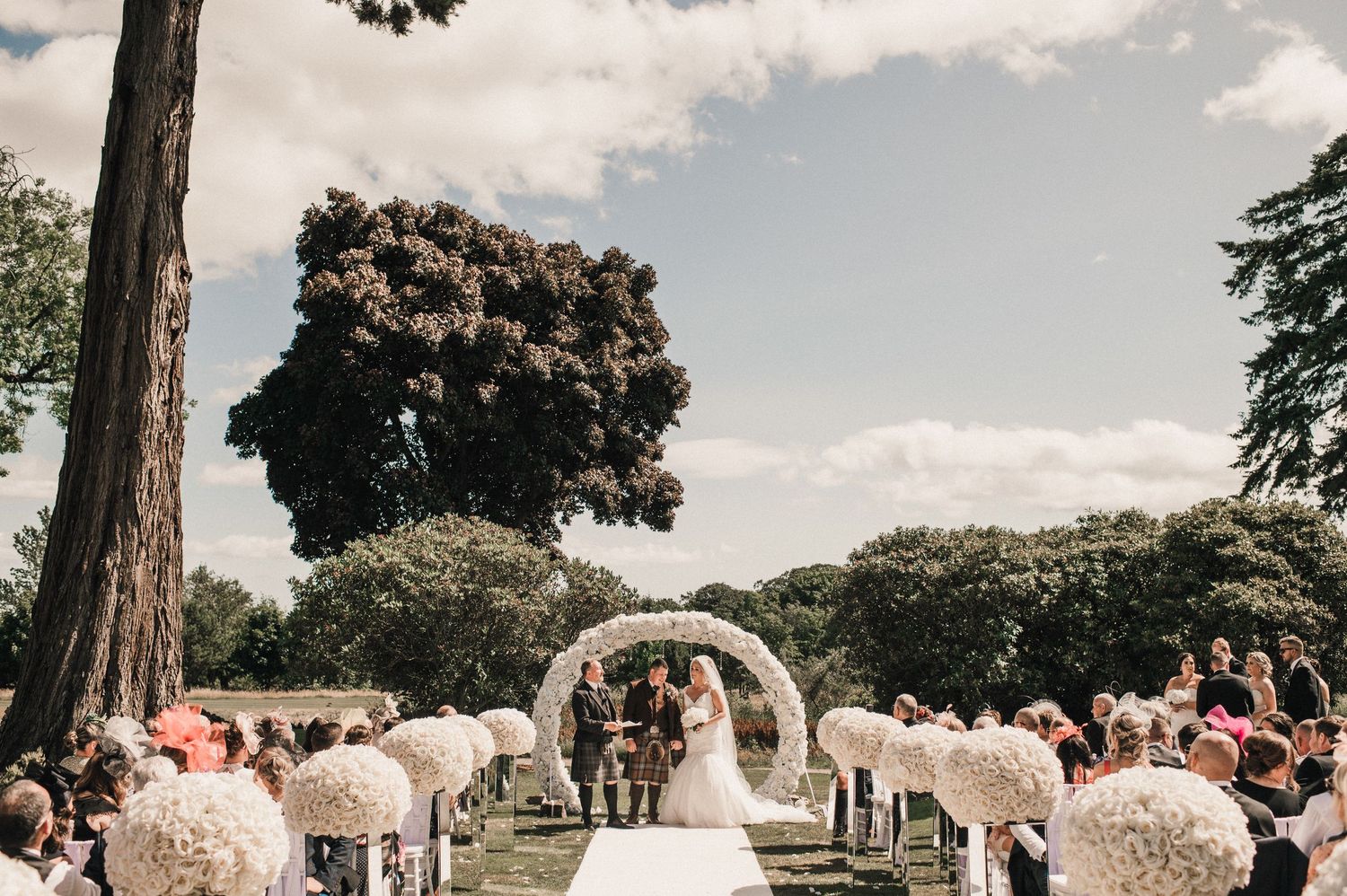 Beautiful outdoor wedding ceremony with white floral arrangements and decorative arch.