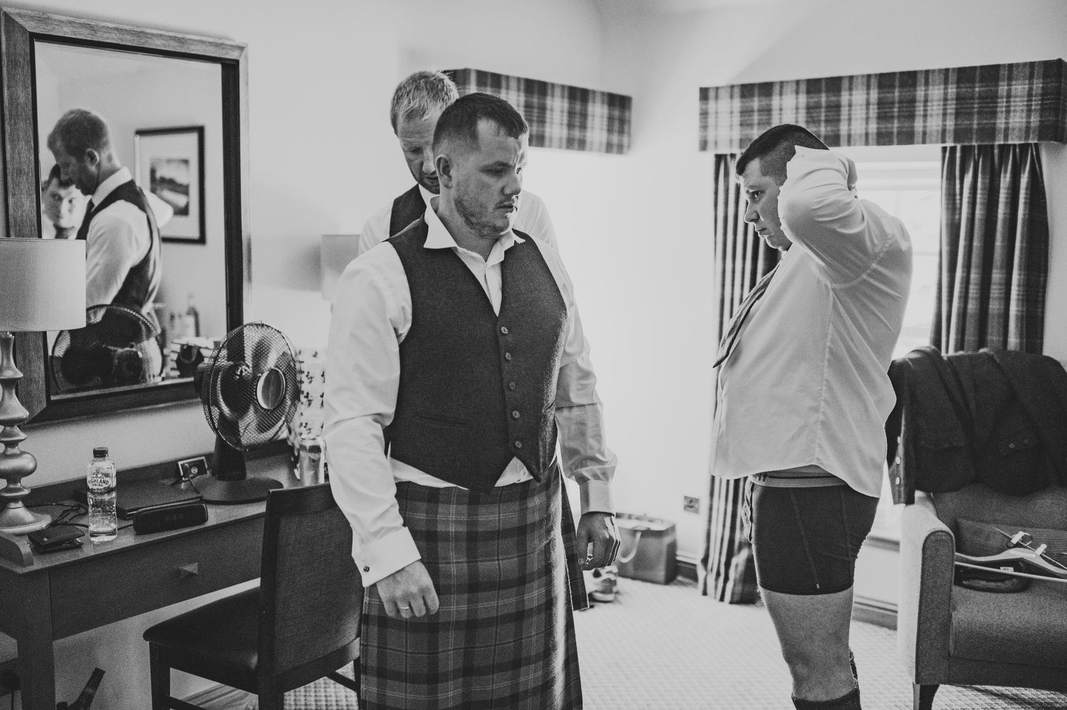 Two people getting ready in formal wear including a traditional kilt and vest.