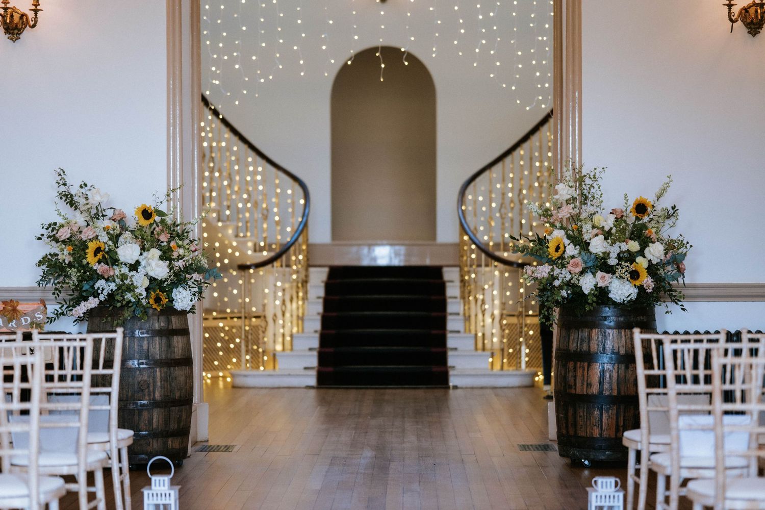 White wedding chairs lined up in rows with twinkling lights and floral arrangements at the altar.