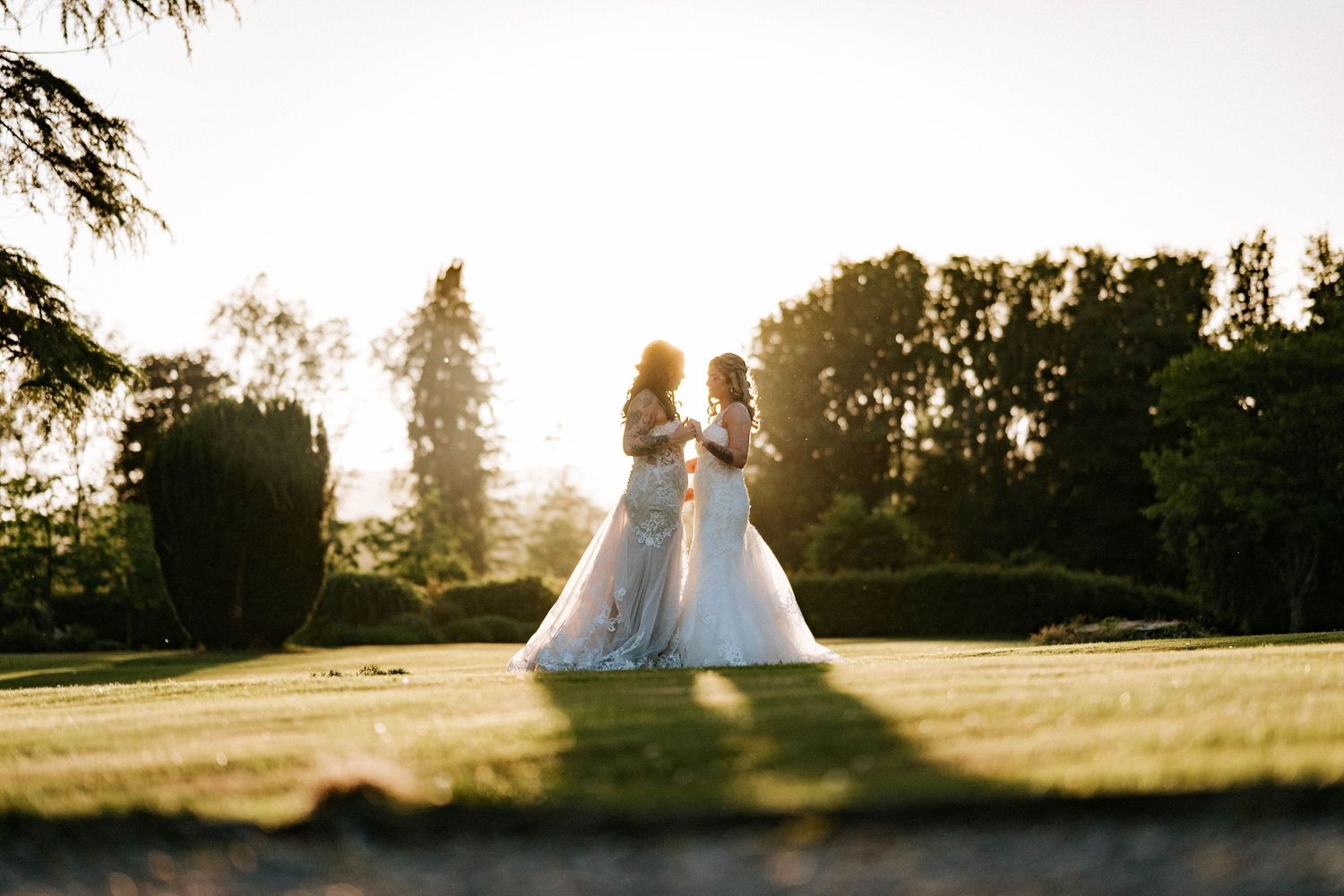 Aberdeen Wedding Photography. Silhouettes of wedding couple in white dresses against setting sun on grassy field.