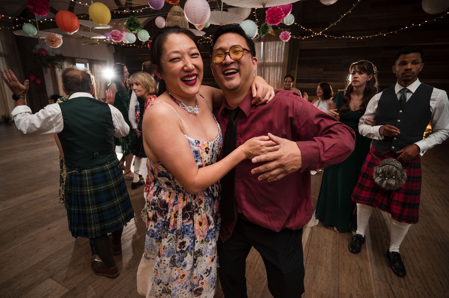 Wedding guests dancing and celebrating on wooden dance floor at evening reception.