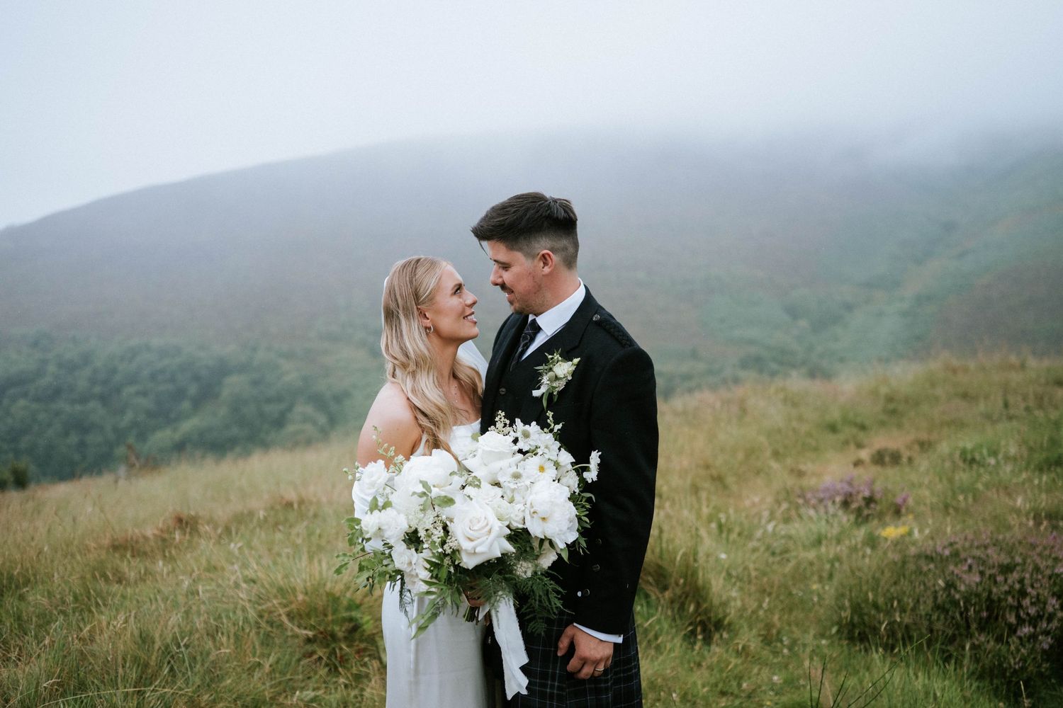 Romantic wedding portraits on a misty hillside with dramatic mountain landscape.