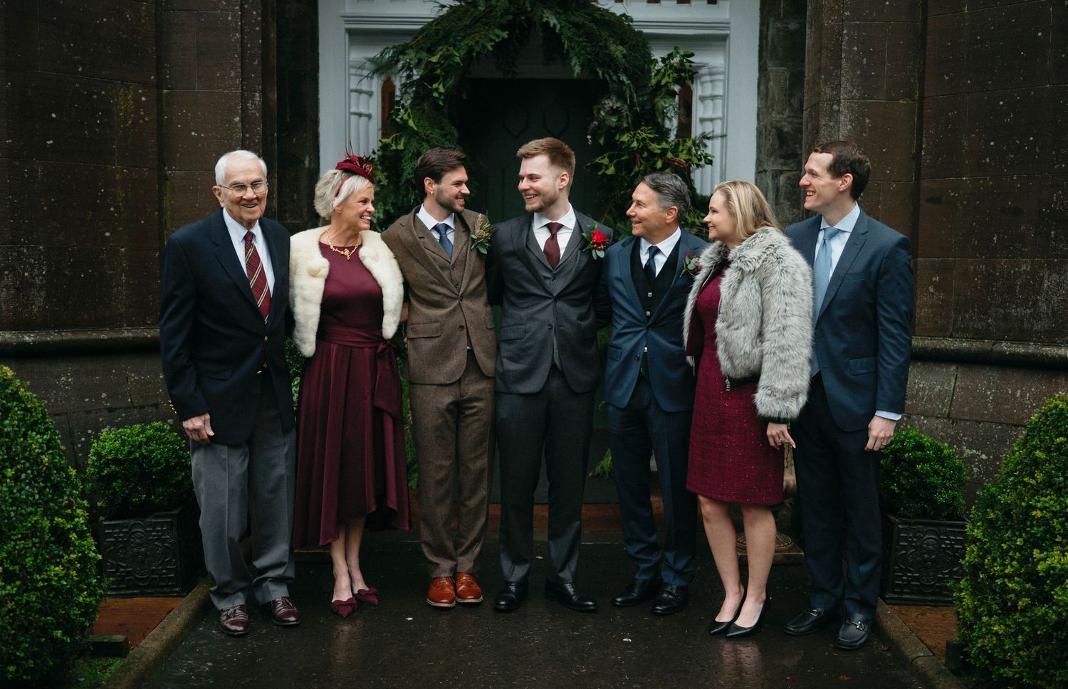 Wedding party gathered in formal attire outside historic brick building entrance.