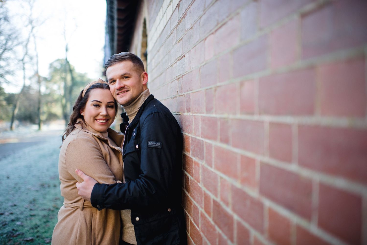 A couple embraces against a brick wall during a winter photoshoot.