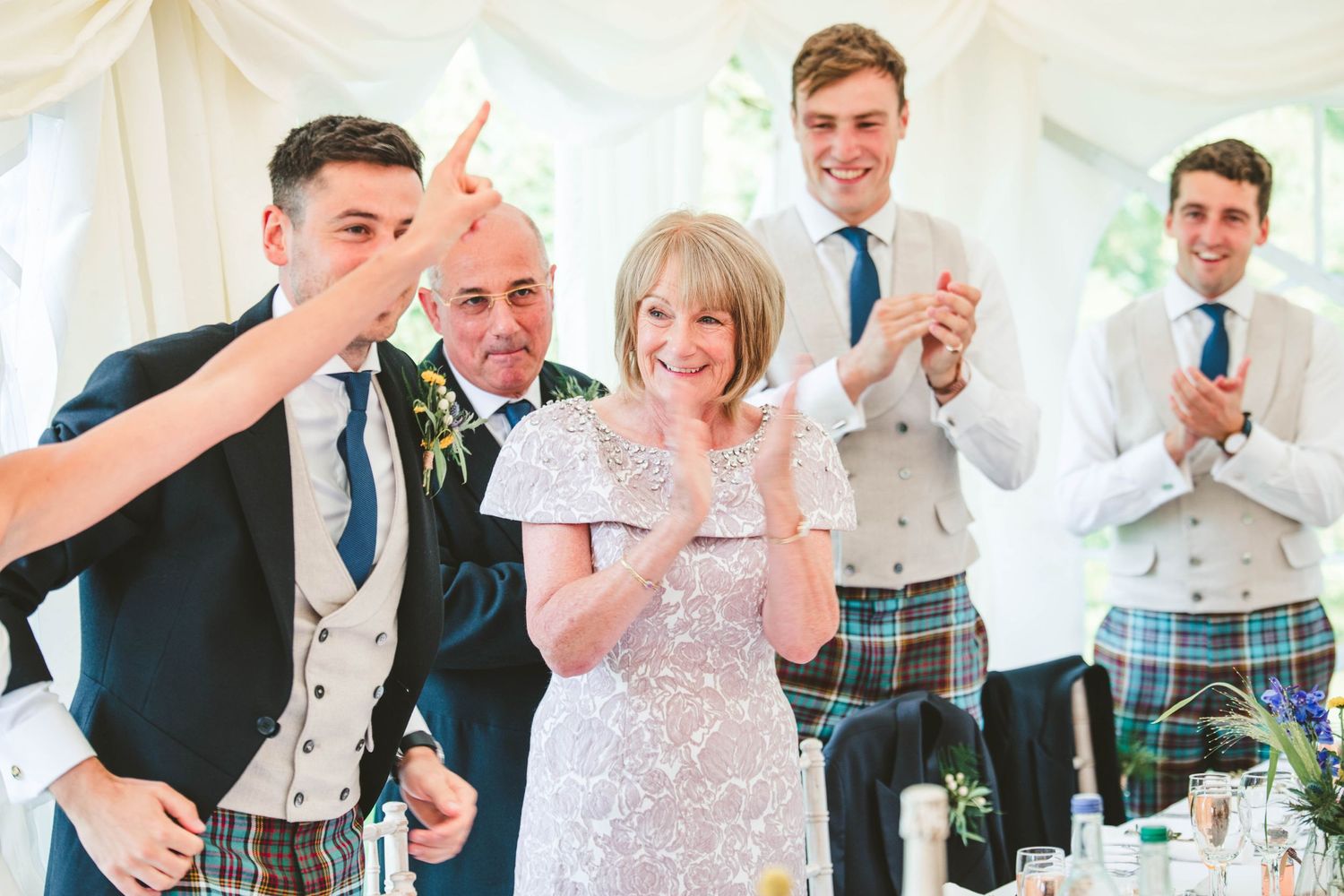 Wedding guests in kilts and formal attire celebrating during reception speeches.