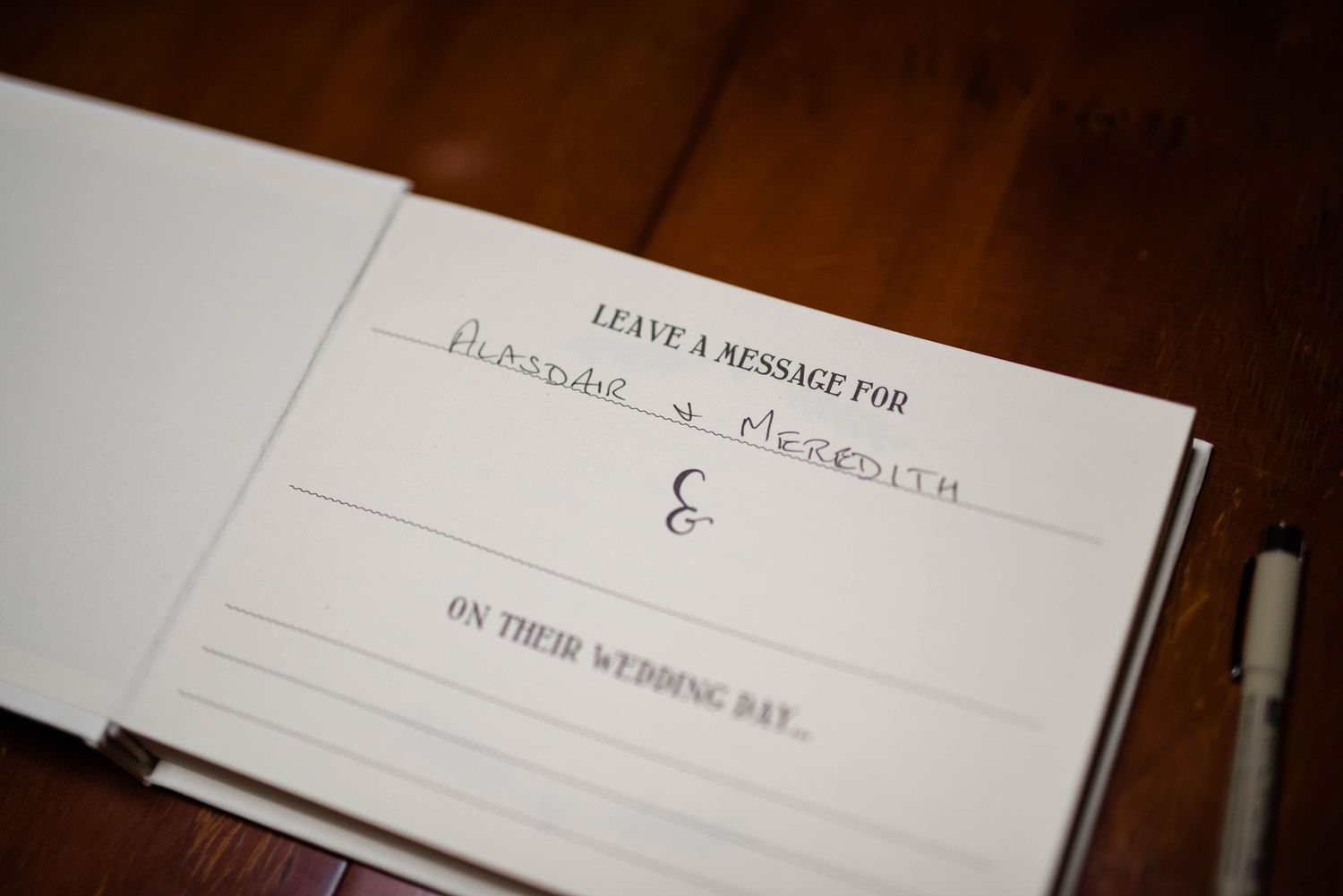 Close-up of a wedding guest book page with 'Leave a message for' text on wooden surface.