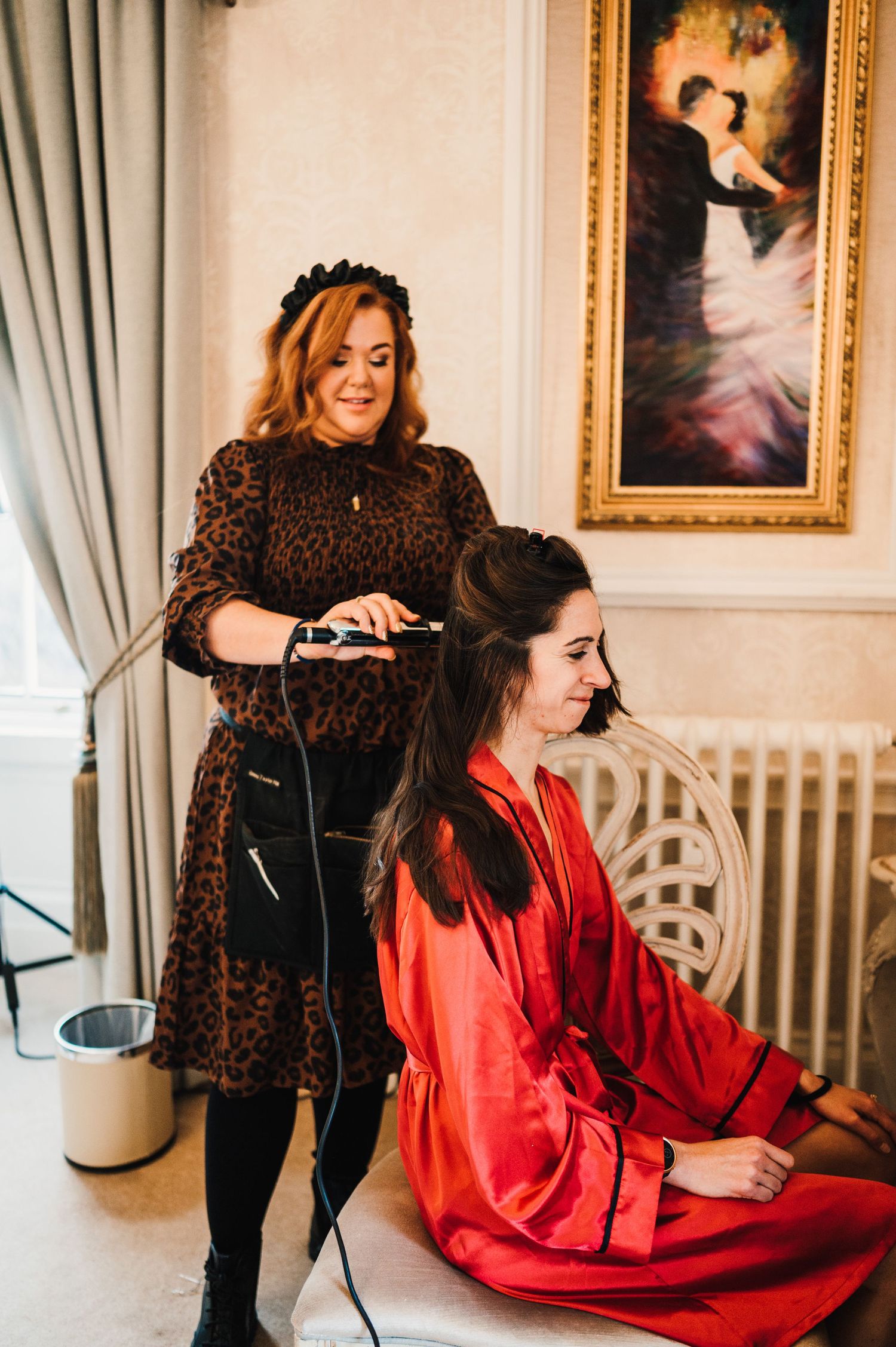 Hair styling session in progress with leopard print dress and red silk robe against classic decor.