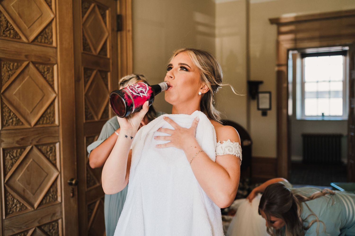 Someone in a white dress takes a sip from a pink soda can before a wedding ceremony.