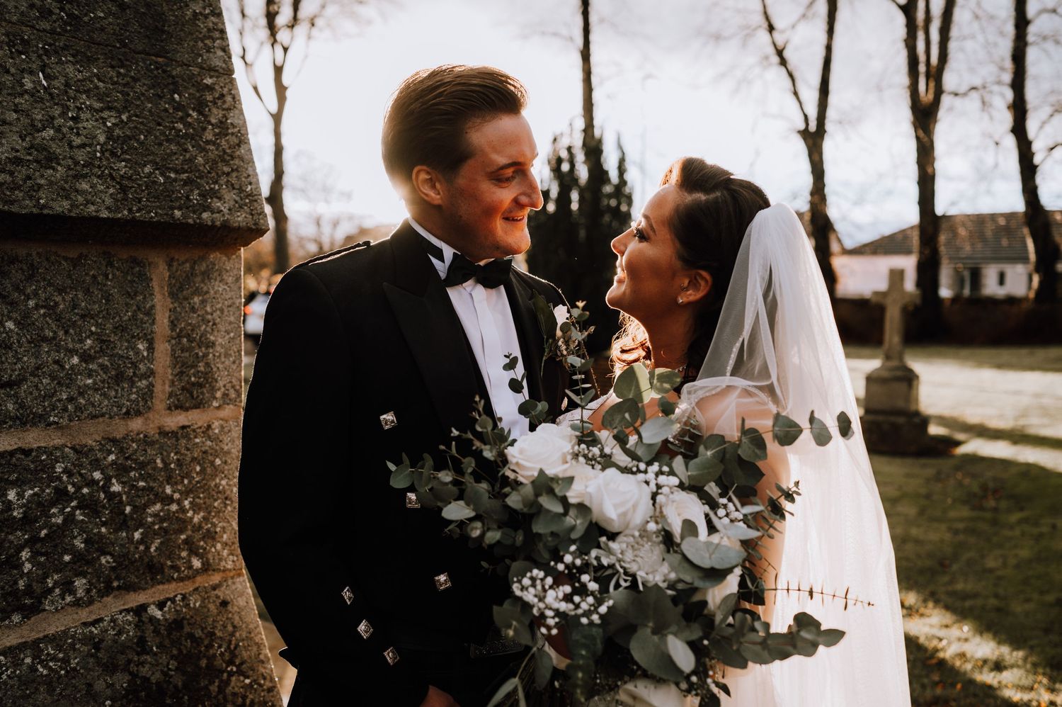 A joyful wedding couple sharing a moment outdoors with their elegant floral bouquet.