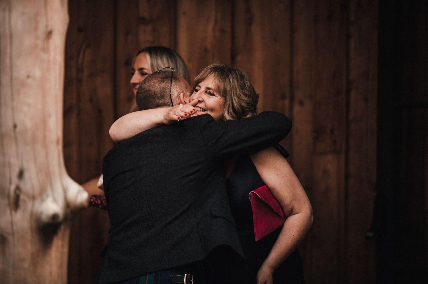 Emotional embrace captured at rustic wooden venue during celebration.
