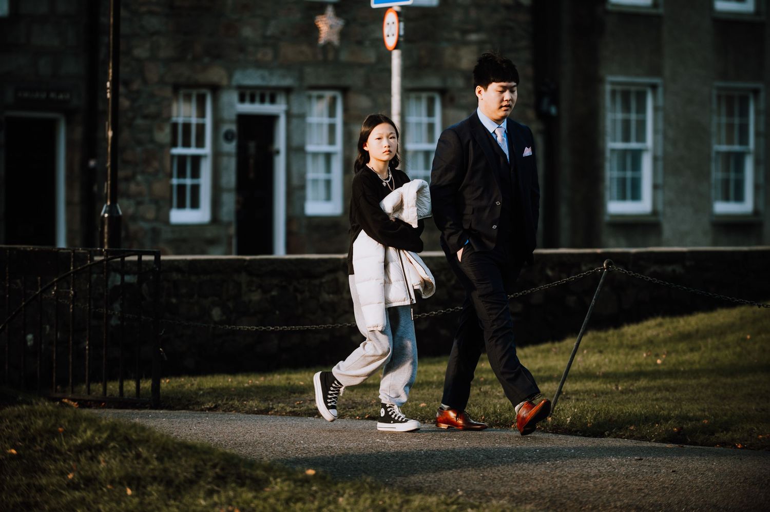 Couple walking outdoors on a path near historic stone buildings.