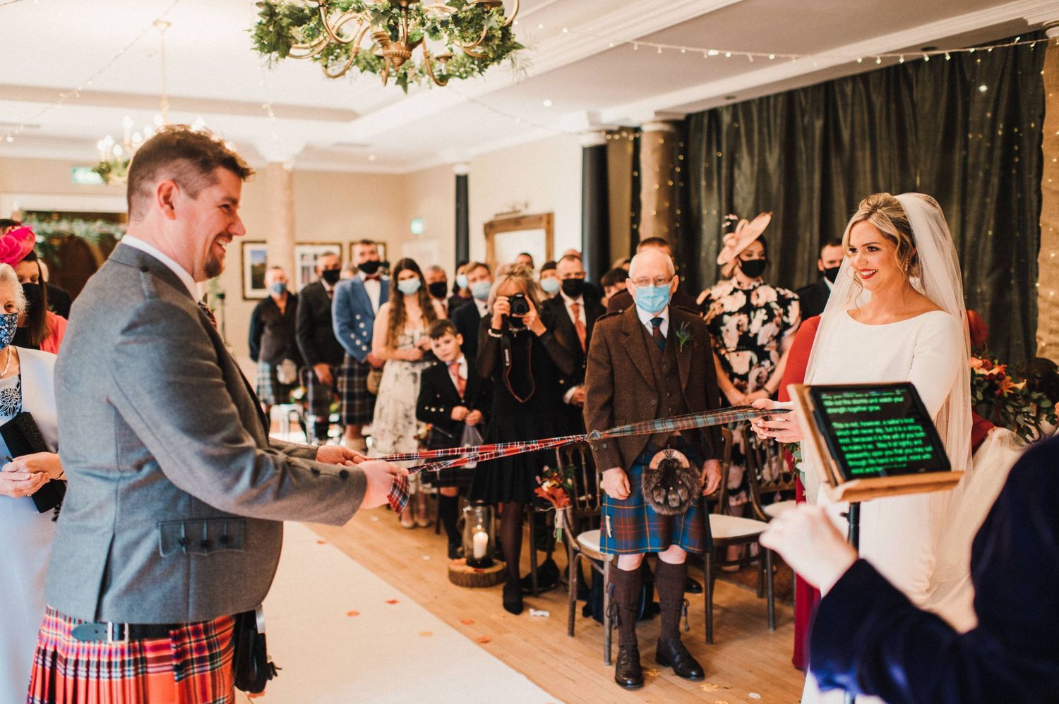 Wedding ceremony with digital tablets and Scottish attire in an elegant ballroom setting.